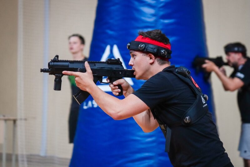 Игрок LASERWAR с автоматом в прицеле у синего препятствия.